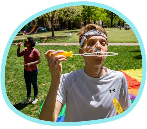 Two students blow bubbles on Polk Place with a colorful parachute on the ground behind them