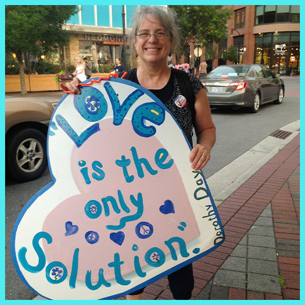Carolina Student Mary Grace holds a heart-shaped sign that reads "Love is the only solution."